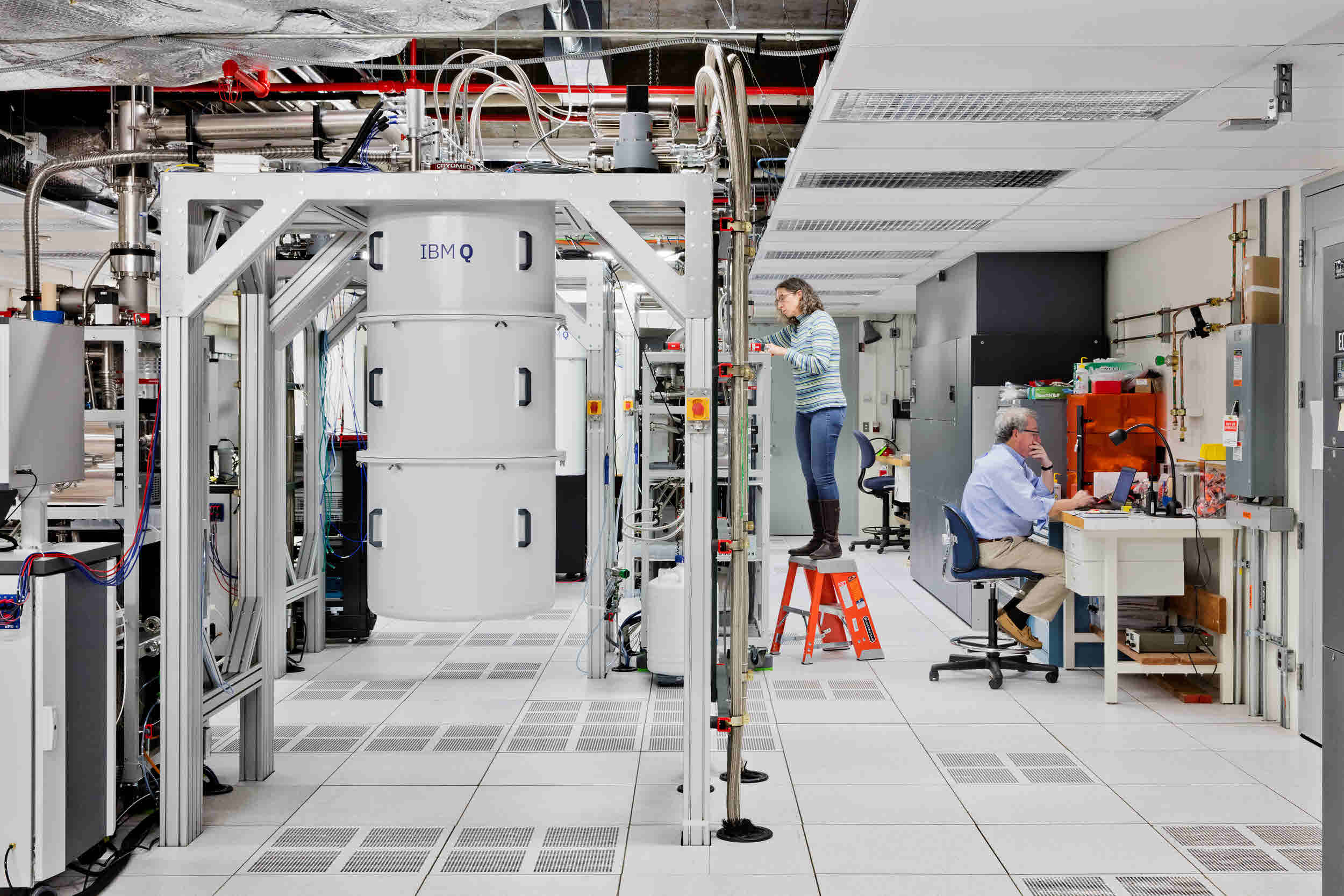IBM superconducting quantum computer lab showing a large white dilution refrigerator with researchers working on control electronics